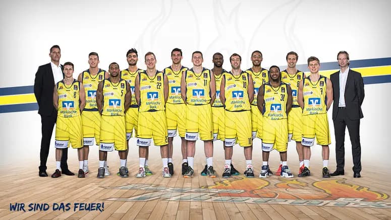 Eine Männer Basketballmannschaft in gelben Trikots lächelt geschlossen auf dem Spielfeld