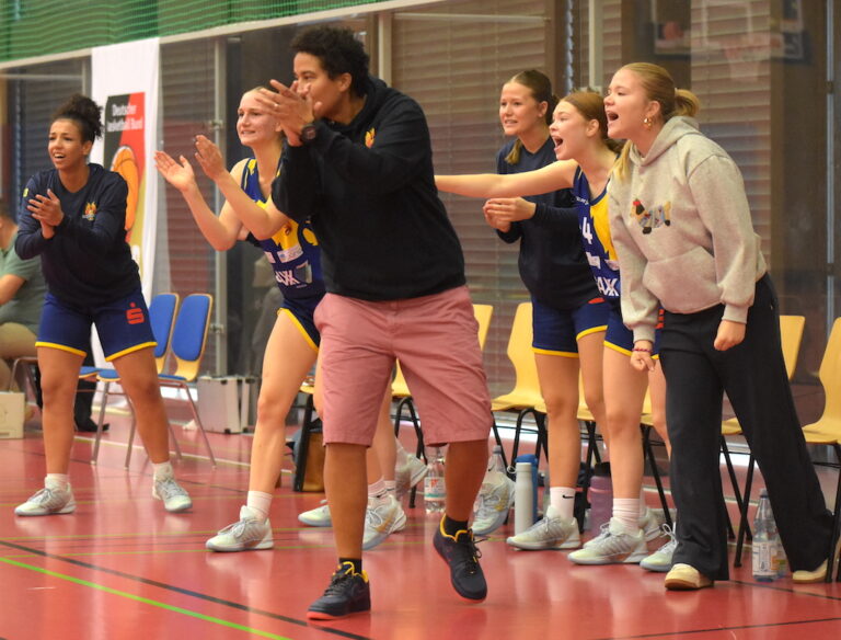 Sechs jubelnde Frauen am Spielfeldrand, sportlich gekleidet, voller Energie und Begeisterung