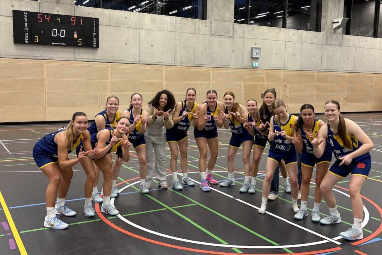 Dreizehn junge Frauen im blauen Sportoutfit lächeln fröhlich und posieren nach einem Spiel