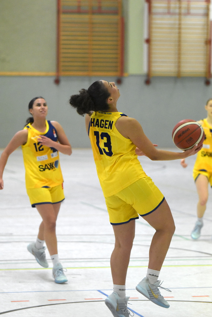 Eine Basketballspielerin im gelben Trikot macht einen Korbleger, konzentriert und dynamisch