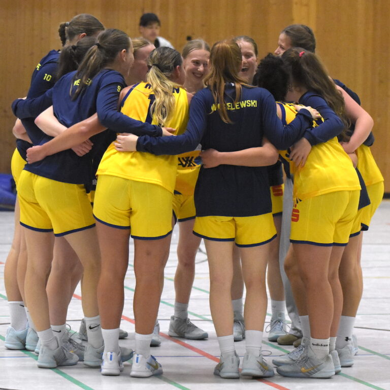 Eine Gruppe junger Frauen im gelben Trikot steht lachend im Kreis und umarmt sich