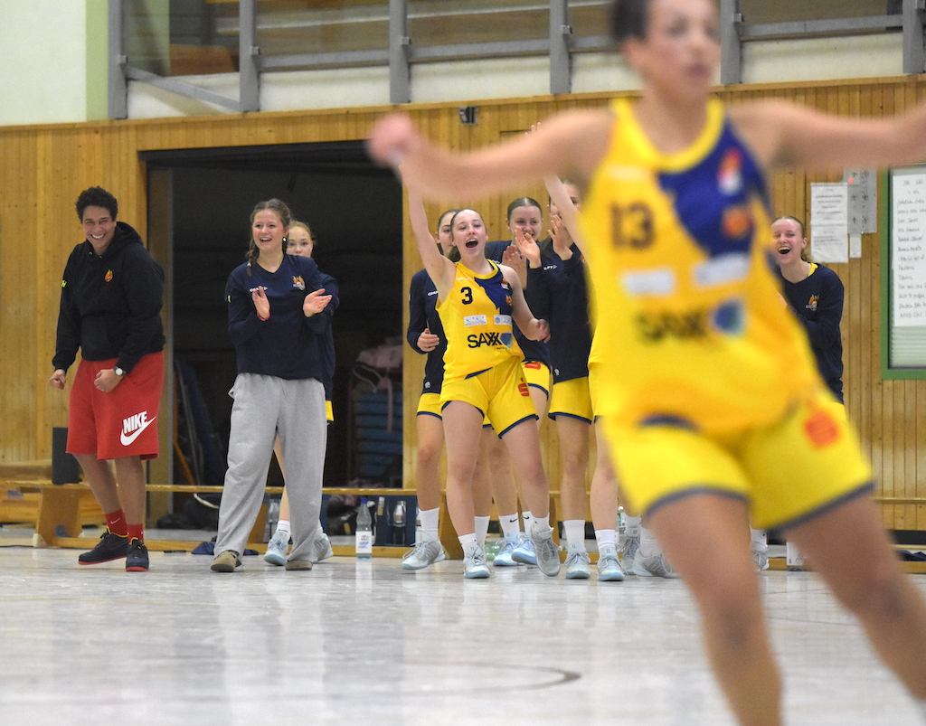 Frauen im gelben Basketballtrikot jubeln fröhlich auf dem Spielfeld mit Begeisterung