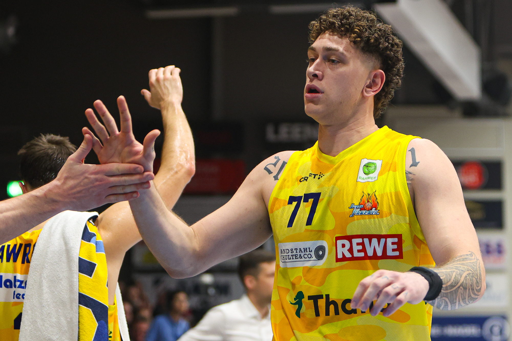 Ein Basketballspieler im gelben Trikot mit lockigen Haaren gibt einem Teamkollegen High Five