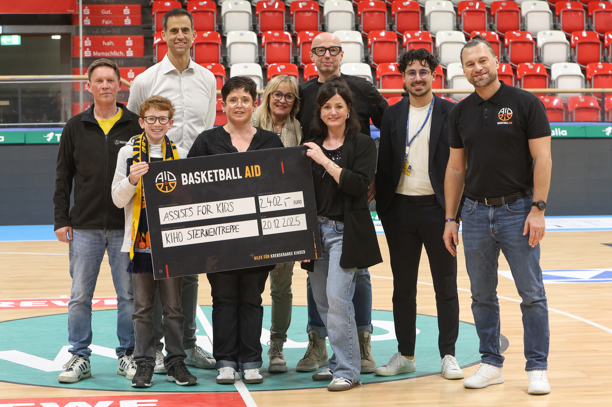 Eine Gruppe lächelnder Menschen hält einen großen Spendenscheck in einer Sporthalle