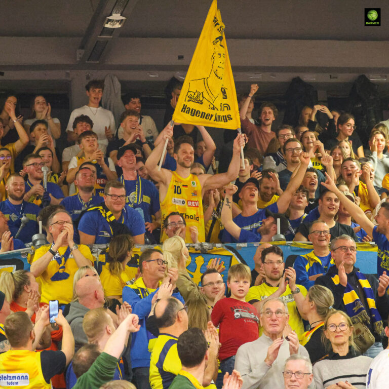 Ein jubelnder Mann im gelben Sporttrikot hält eine gelbe Fahne in einer Menschenmenge