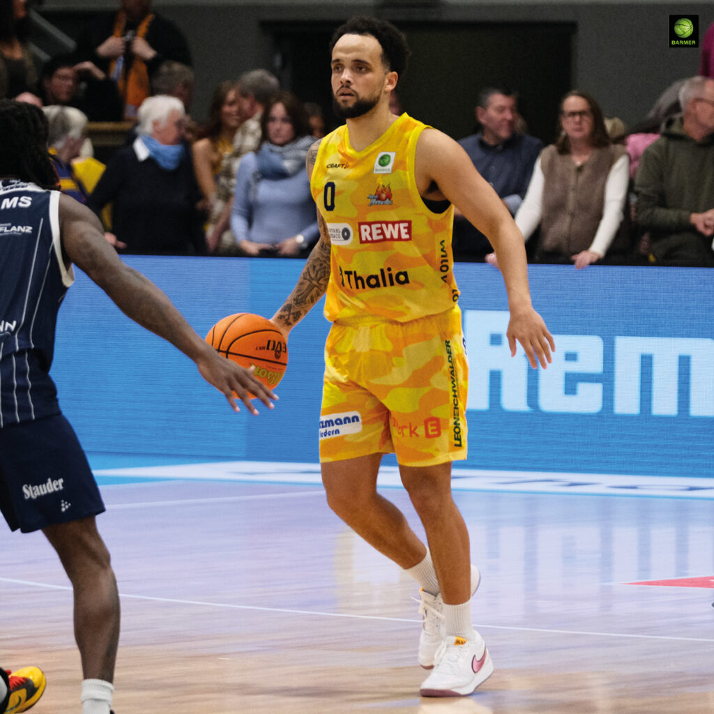 Ein fokussierter Basketballspieler im gelben Trikot hält einen orangefarbenen Ball