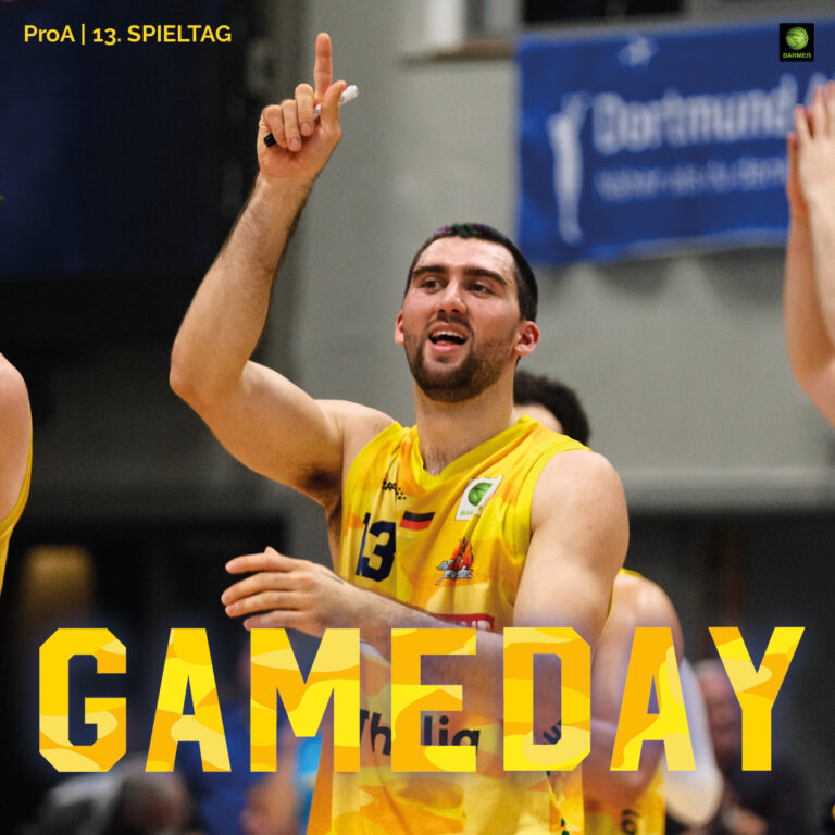 Ein jubelnder Basketballspieler im gelben Trikot mit erhobenem Finger und breitem Lächeln