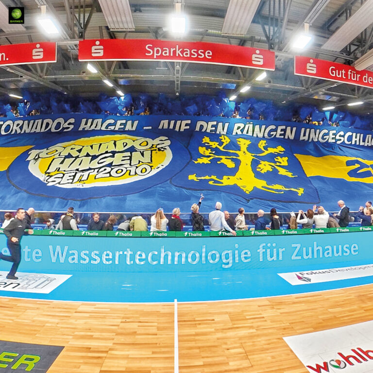 Jubelnde Fans mit riesigem blaugelben Banner und Löwenmotiv in der Sporthalle