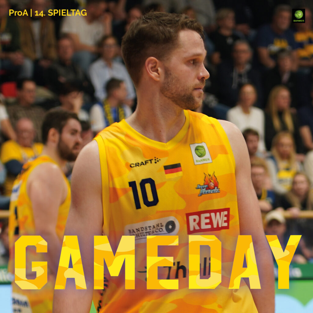 Basketballspieler im gelben Trikot mit ernstem Blick vor unscharfem Zuschauerrang