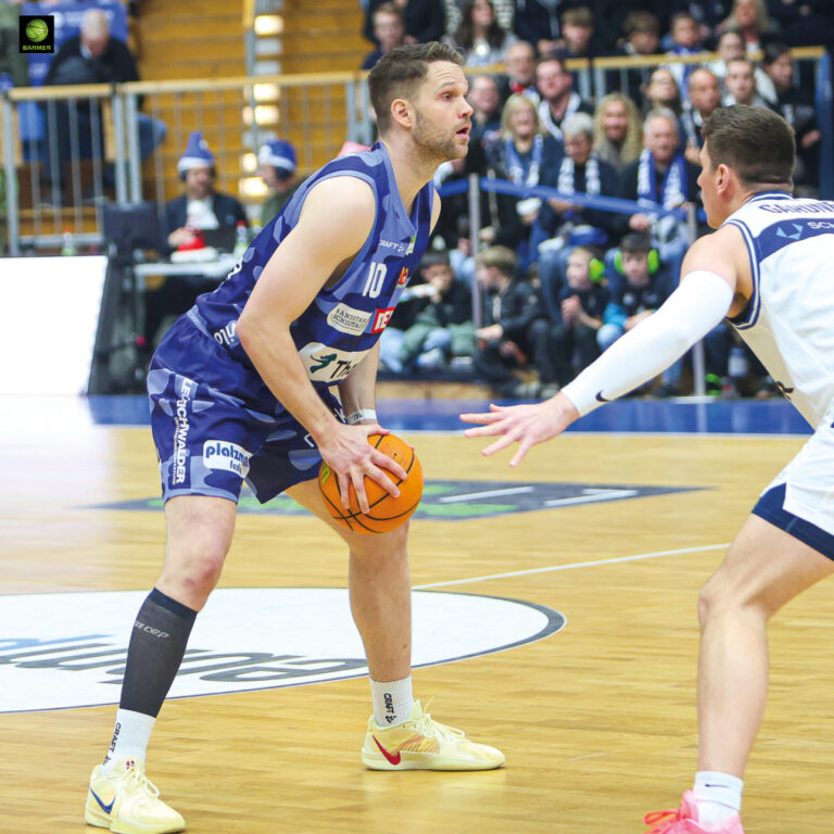 Zwei Basketballspieler im Spiel, einer in Lila konzentriert mit orangefarbenem Ball