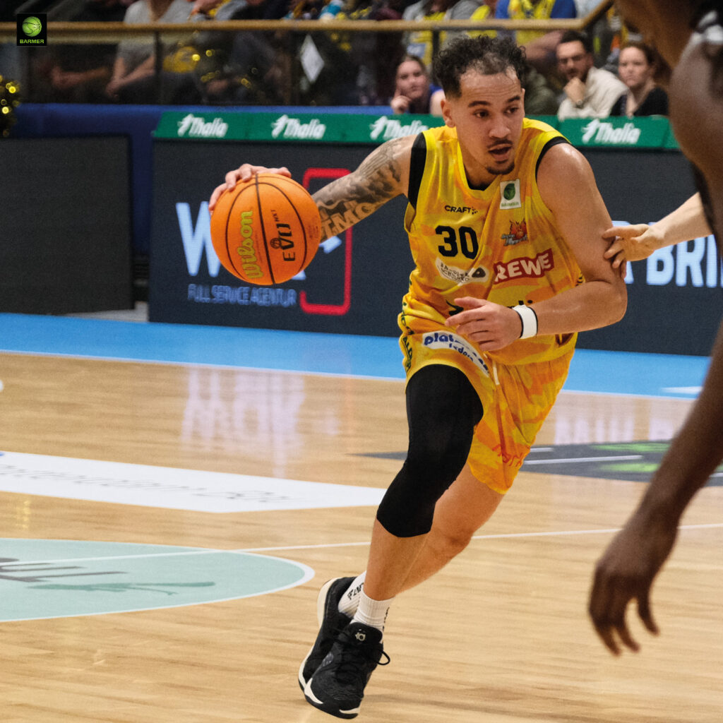 Ein Basketballspieler im gelben Trikot dribbelt konzentriert über das Spielfeld