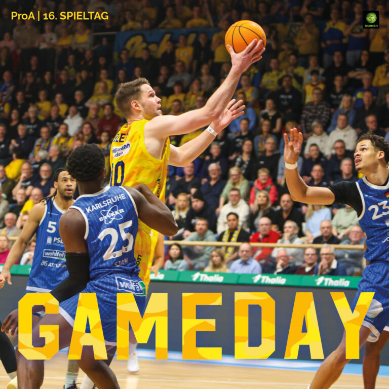 Ein Basketballspieler im gelben Trikot springt dynamisch mit konzentriertem Gesichtsausdruck zum Korb, während zwei Gegner in blauen Trikots versuchen ihn zu stoppen