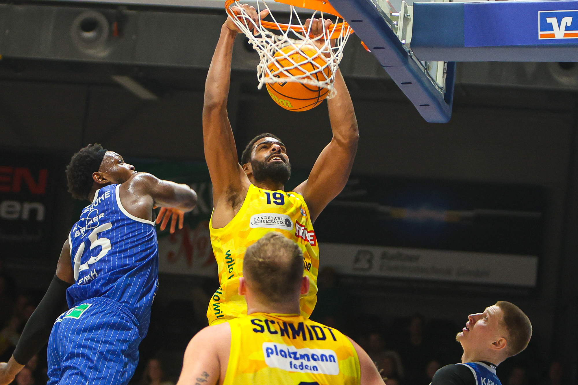 Ein Basketballspieler im gelben Trikot dunkt konzentriert den Ball in den Korb