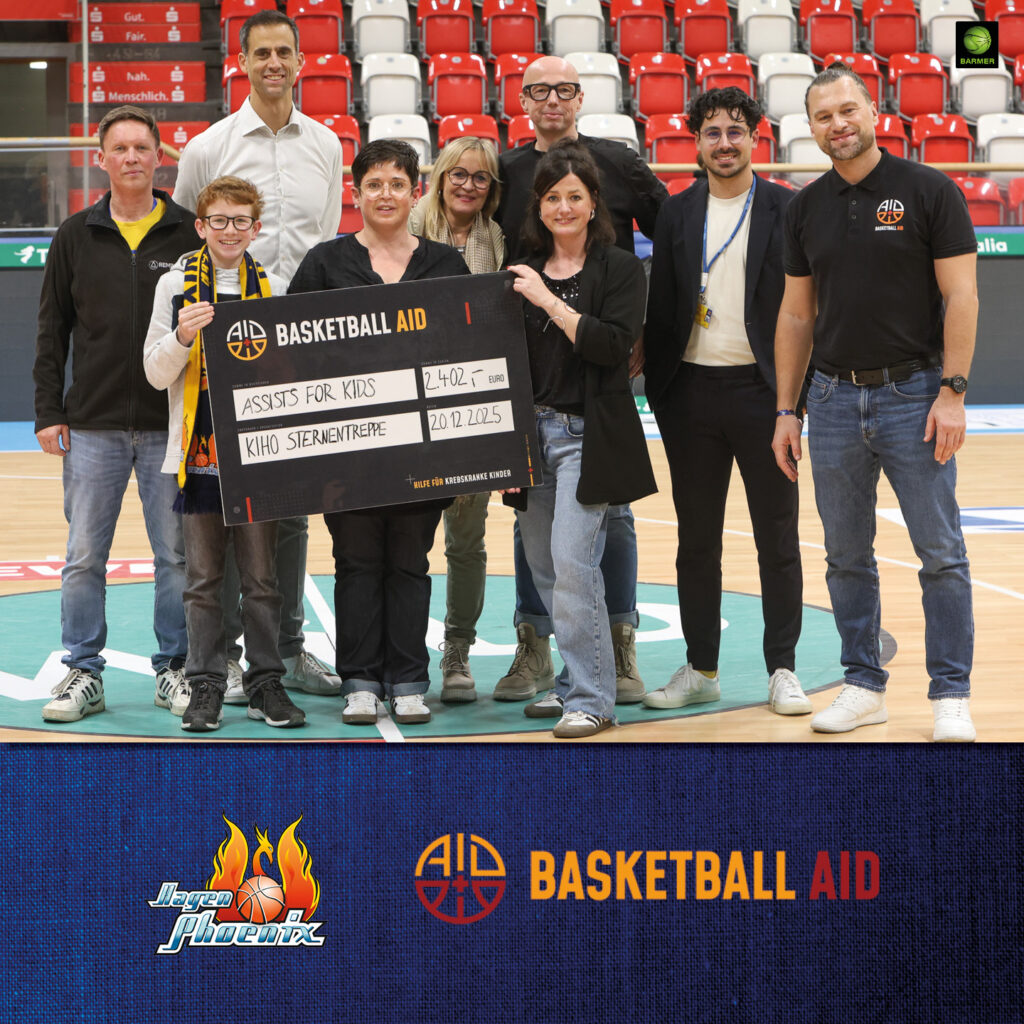 Eine gemischte Gruppe lachender Menschen hält einen großen Scheck auf einem Basketballfeld