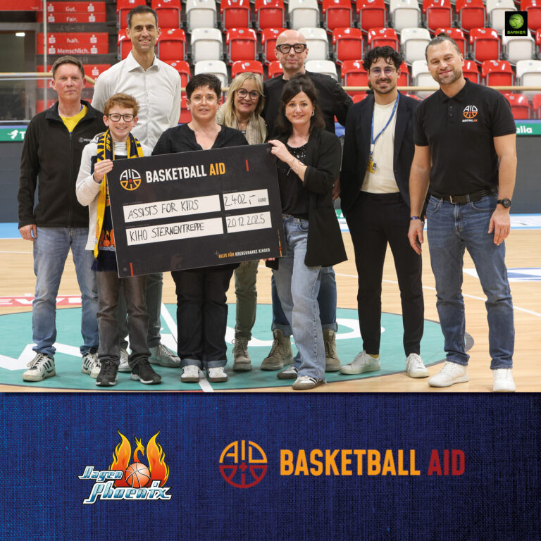 Eine gemischte Gruppe lachender Menschen hält einen großen Scheck auf einem Basketballfeld