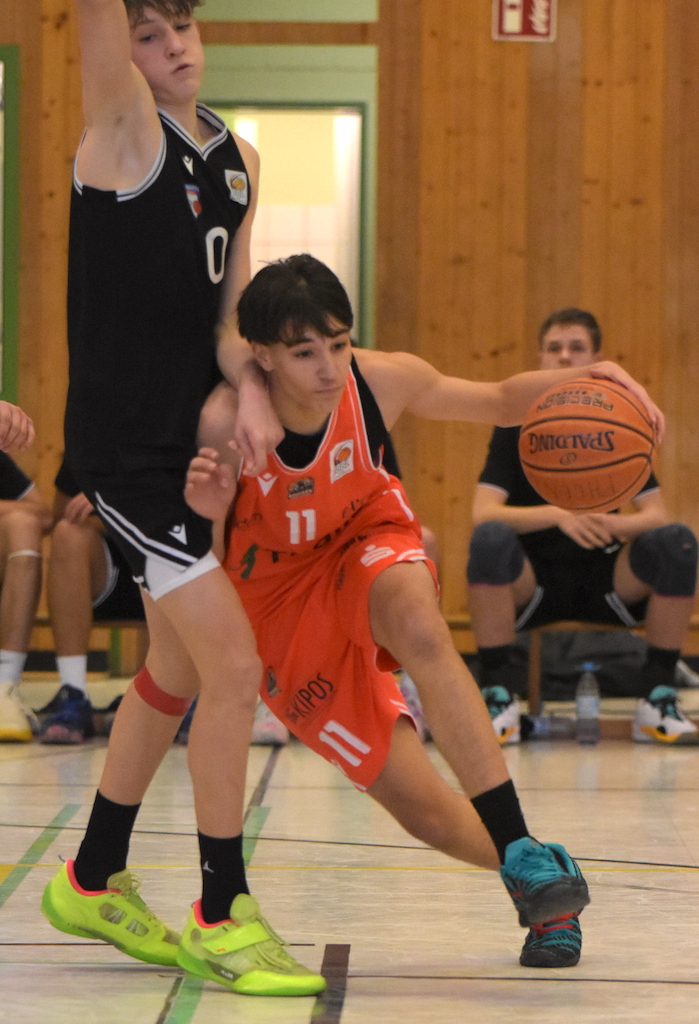 Ein jugendlicher Basketballspieler im orangen Trikot dribbelt konzentriert am Gegner vorbei