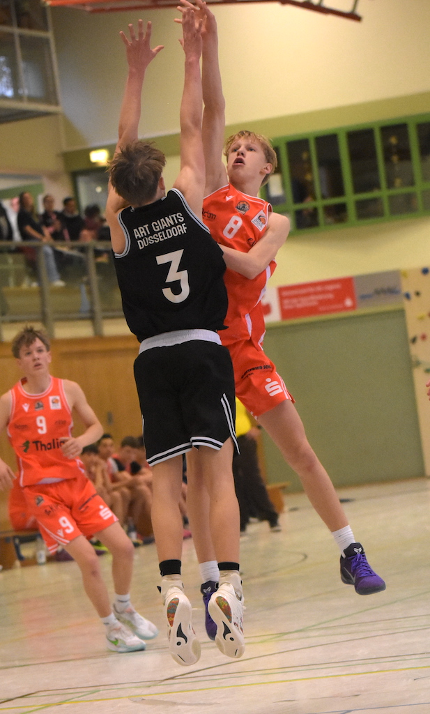 Zwei jugendliche Basketballspieler springen energisch gegeneinander, einer trägt Orange