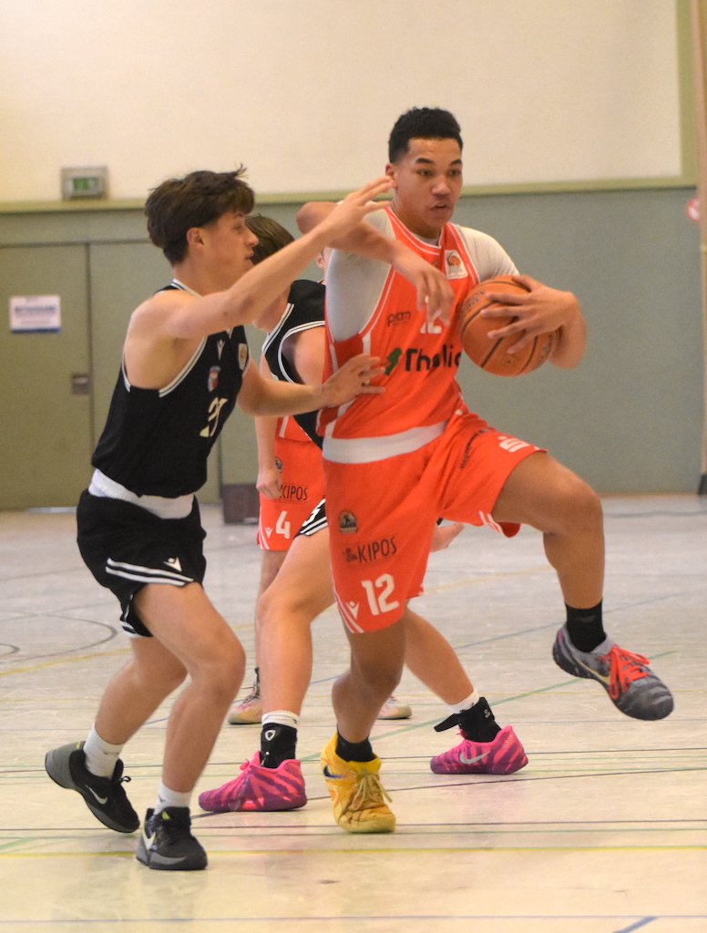 Zwei junge Basketballspieler im Spiel, einer in Orange mit entschlossenem Blick und Ball