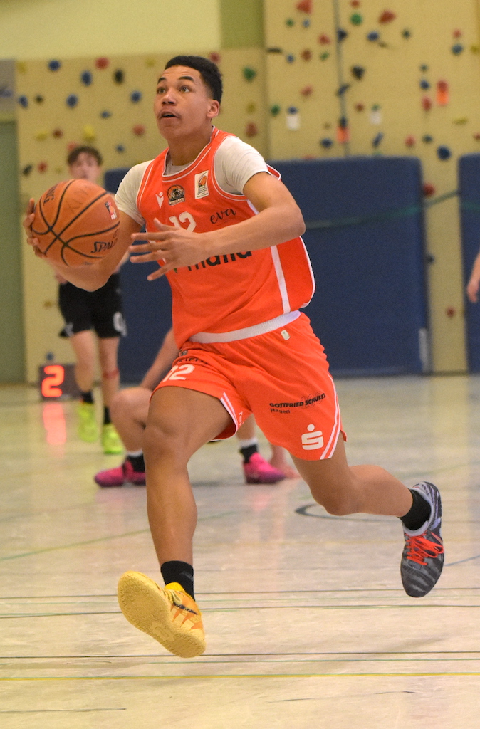 Ein junger Basketballspieler im orangefarbenen Trikot zieht fokussiert zum Korb