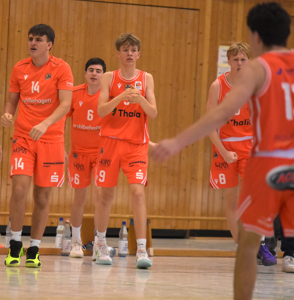 Vier jugendliche Basketballspieler in orangefarbenen Trikots schauen konzentriert