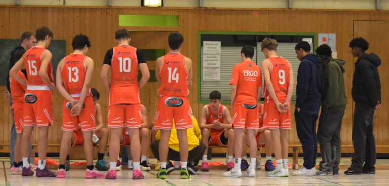 Eine Basketballmannschaft in orangefarbenen Trikots bespricht sich aufmerksam in der Halle
