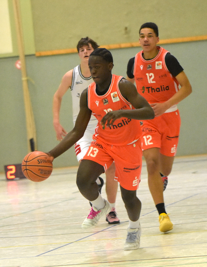 Ein junger Basketballspieler im orangefarbenen Trikot läuft konzentriert mit dem Ball