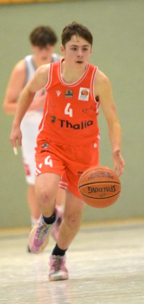 Junger Basketballspieler mit konzentriertem Gesichtsausdruck in oranger Uniform beim Dribbeln
