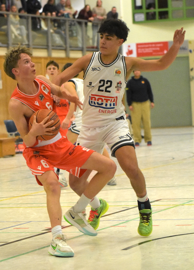Zwei junge Basketballspieler in weißen und orangefarbenen Trikots im Spiel mit angespannter Miene