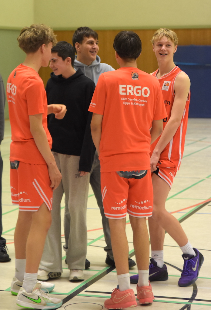 Vier junge Männer in roten Basketballtrikots lachen und unterhalten sich gemeinsam
