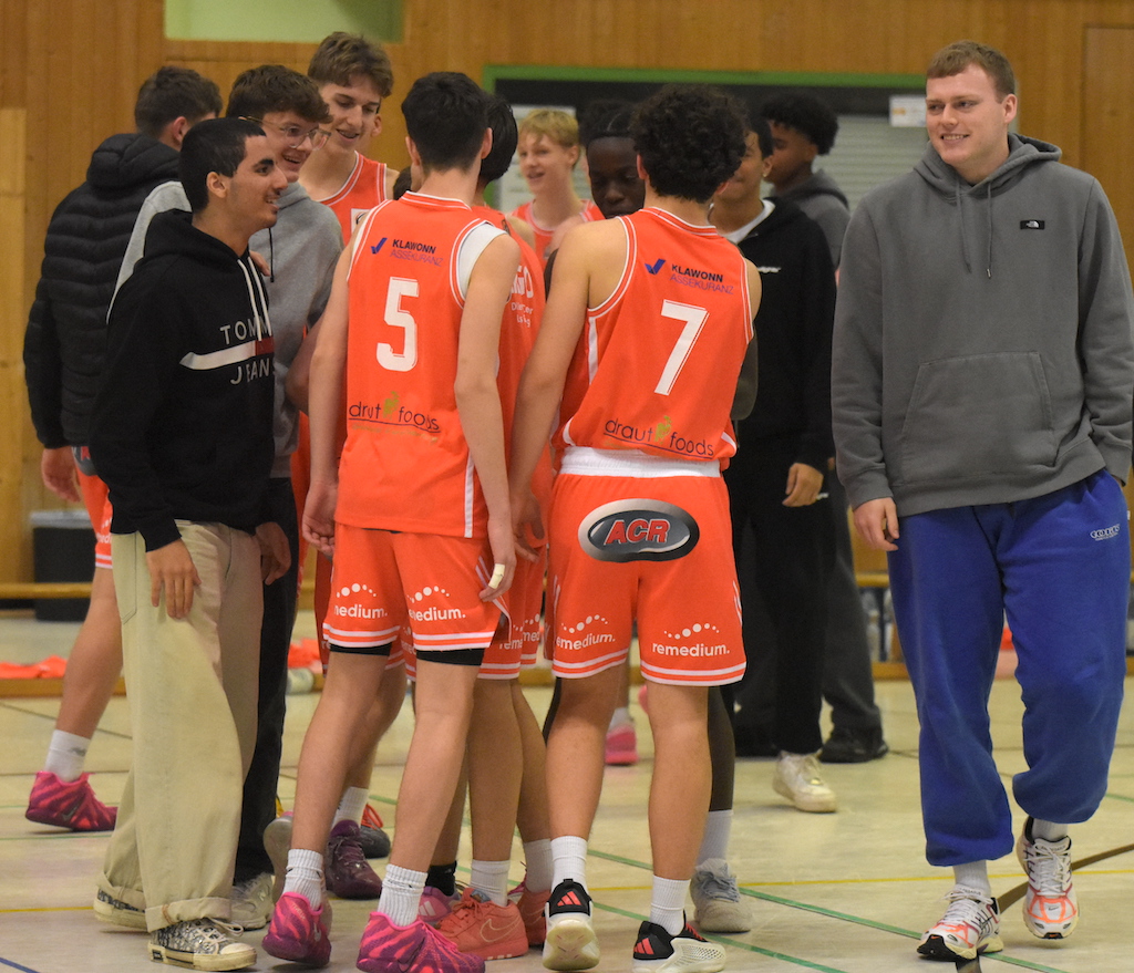 Junge Männer im orangenen Basketballtrikot stehen lachend in einer Sporthalle zusammen