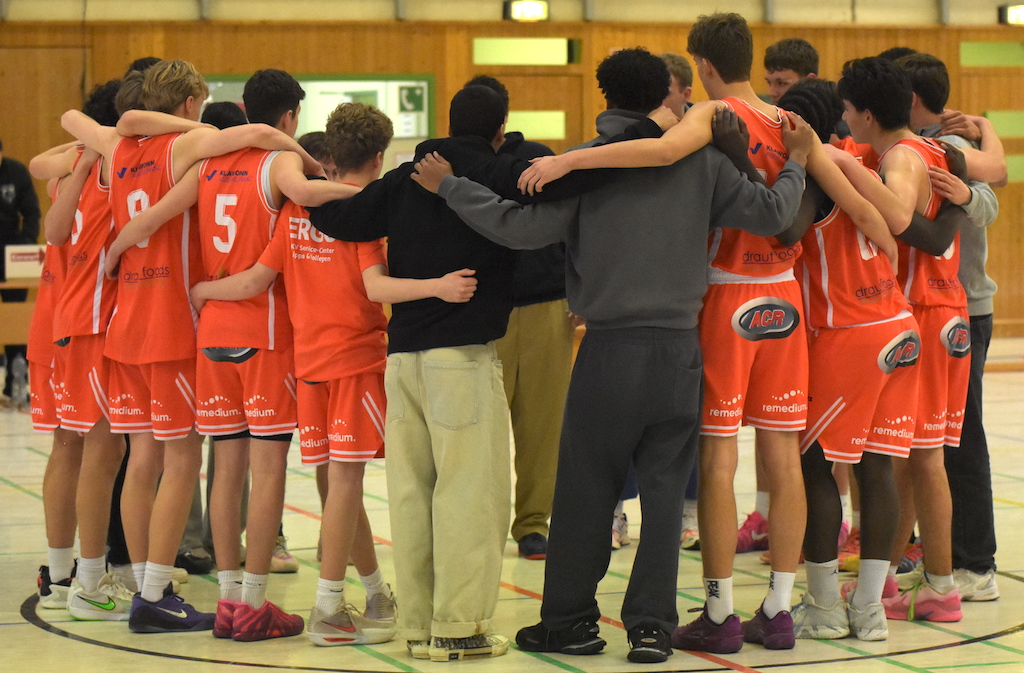 Eine Basketballmannschaft in orangefarbenen Trikots steht im Kreis und wirkt konzentriert
