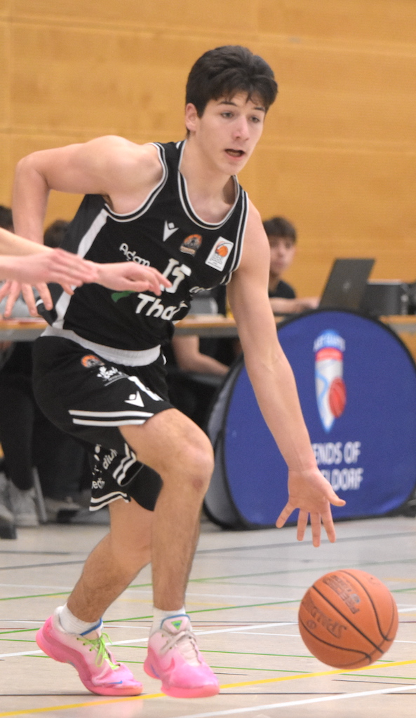 Junger Basketballspieler mit fokussiertem Blick dribbelt in schwarzem Trikot und pinken Schuhen