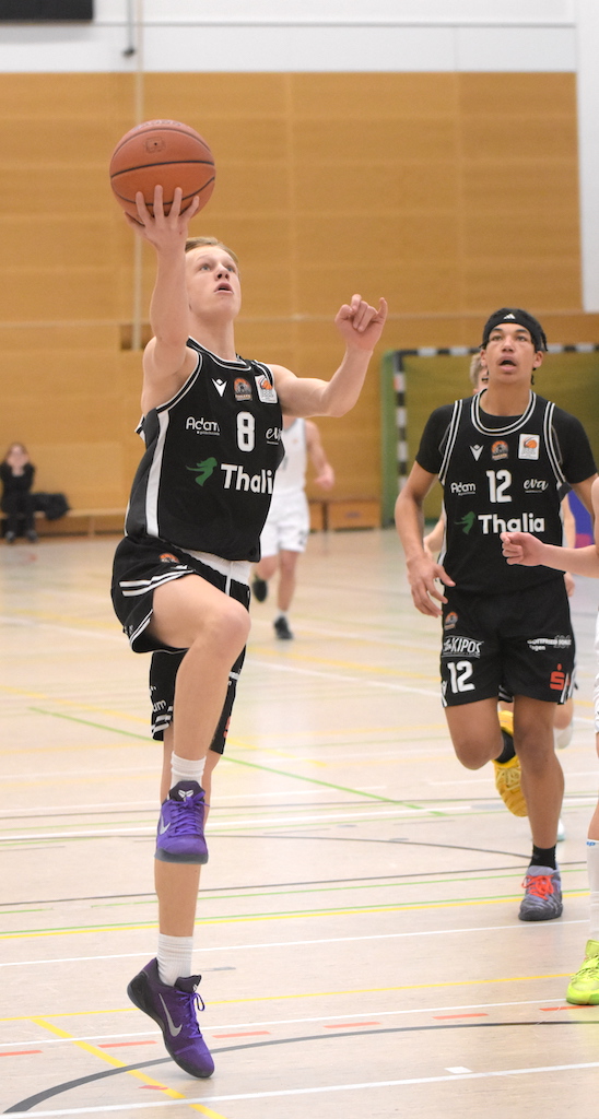 Ein blonder Jugendlicher im schwarzen Basketballtrikot springt dynamisch zum Korb