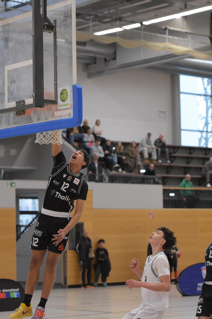 Ein Basketballspieler im schwarzen Trikot jubelt beim Korbleger, ein Gegner schaut zu