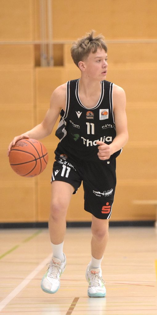 Junger Basketballspieler mit konzentriertem Blick im schwarzen Trikot dribbelt den Ball