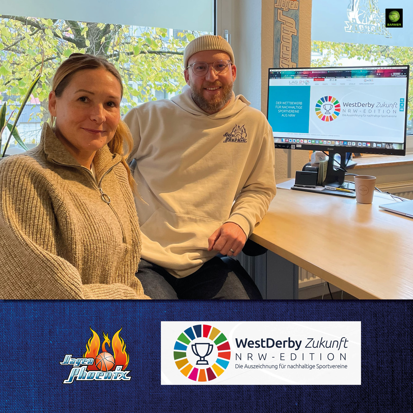 Eine Frau und ein Mann sitzen lächelnd vor einem Computer mit buntem Logo auf dem Bildschirm