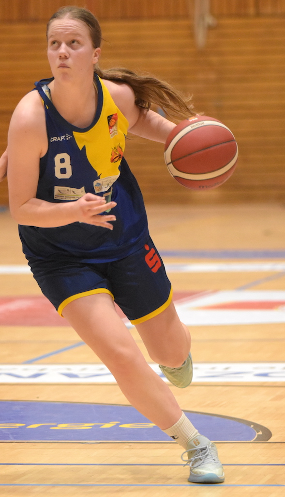 Junge Frau im blauen Basketballtrikot dribbelt konzentriert mit einem Basketball