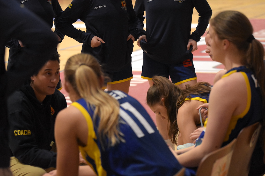 Eine Trainerin spricht motivierend zu Basketballspielerinnen im blauen Trikot
