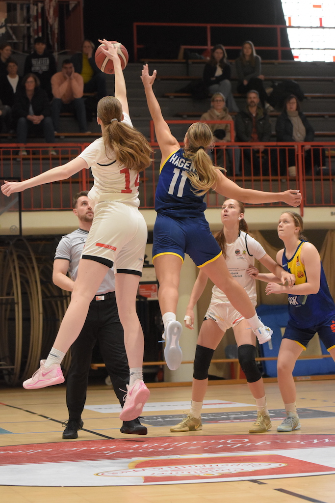 Zwei Basketballspielerinnen springen dynamisch zum Ball, voller Energie und Spannung