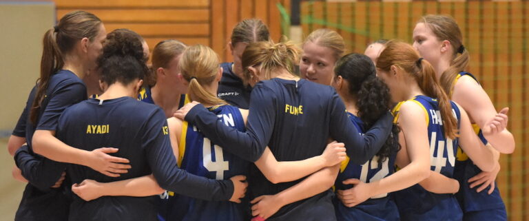 Mehrere junge Frauen mit ernsten Gesichtern umarmen sich im blauen Sporttrikot