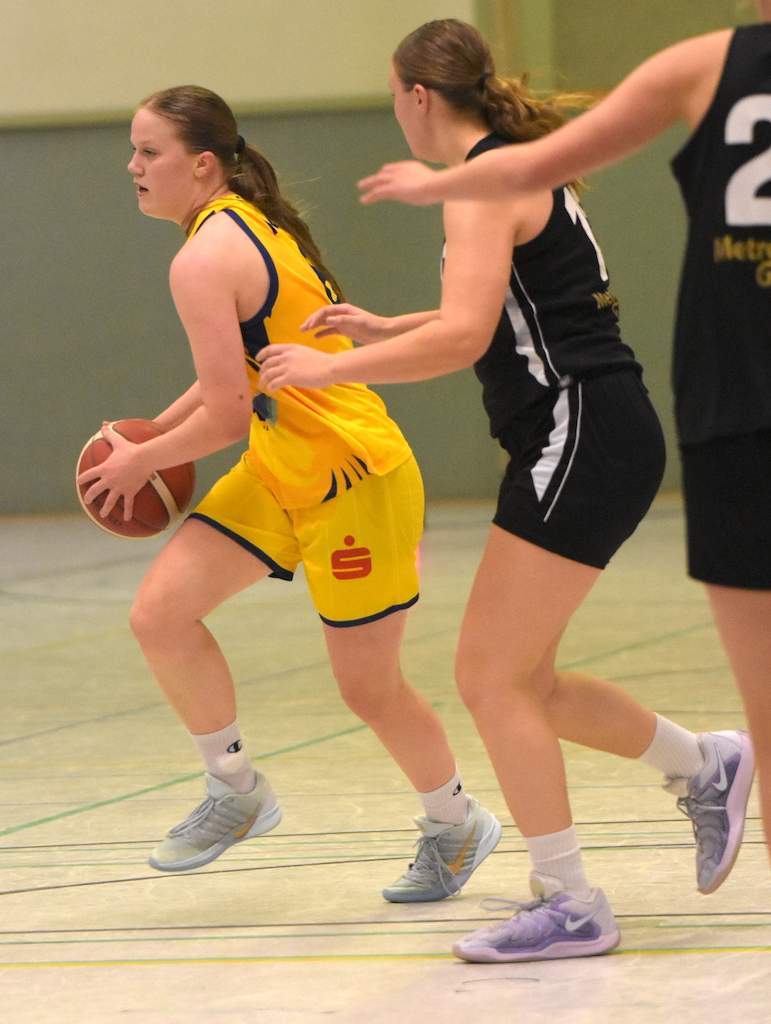 Zwei junge Frauen spielen Basketball in gelb und schwarz, beide konzentriert und aktiv