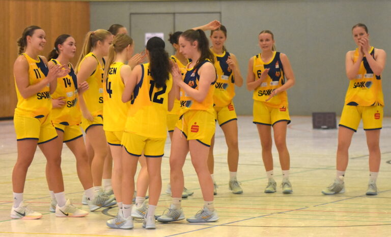Eine Gruppe junger Frauen im gelben Basketballtrikot klatscht lachend in der Halle