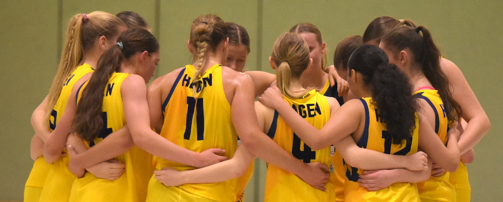 Eine Gruppe junger Frauen in gelben Basketballtrikots steht im Kreis und wirkt konzentriert