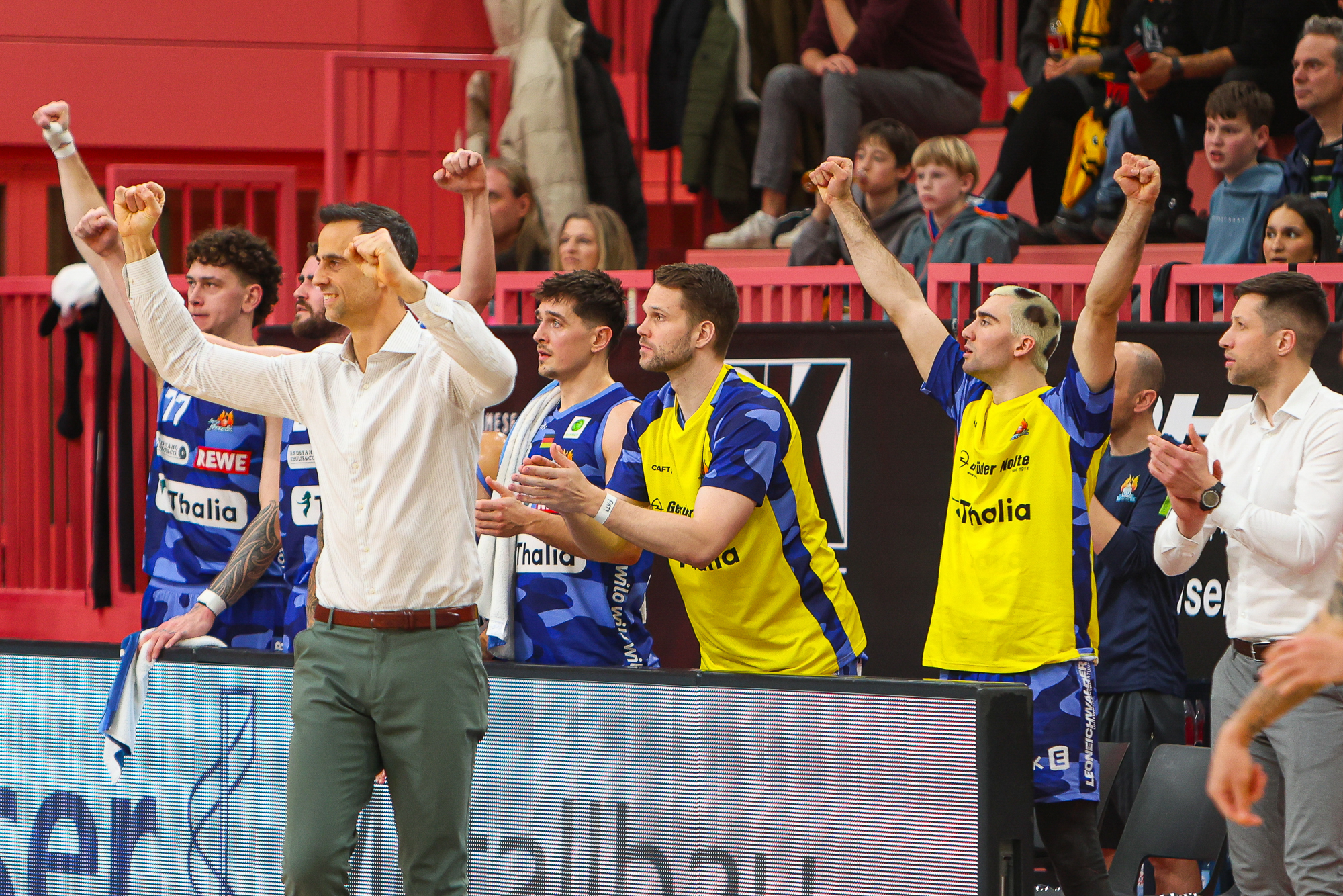 Ein begeistertes Handballteam in blauen und gelben Trikots jubelt mit erhobenen Armen