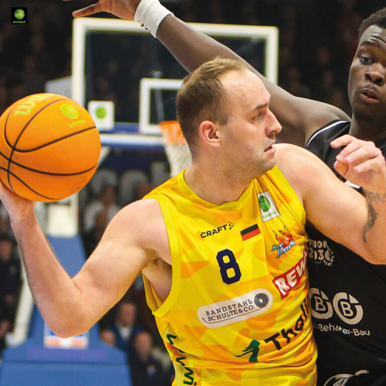 Ein Basketballspieler mit entschlossenem Blick im gelben Trikot hält den Ball fest