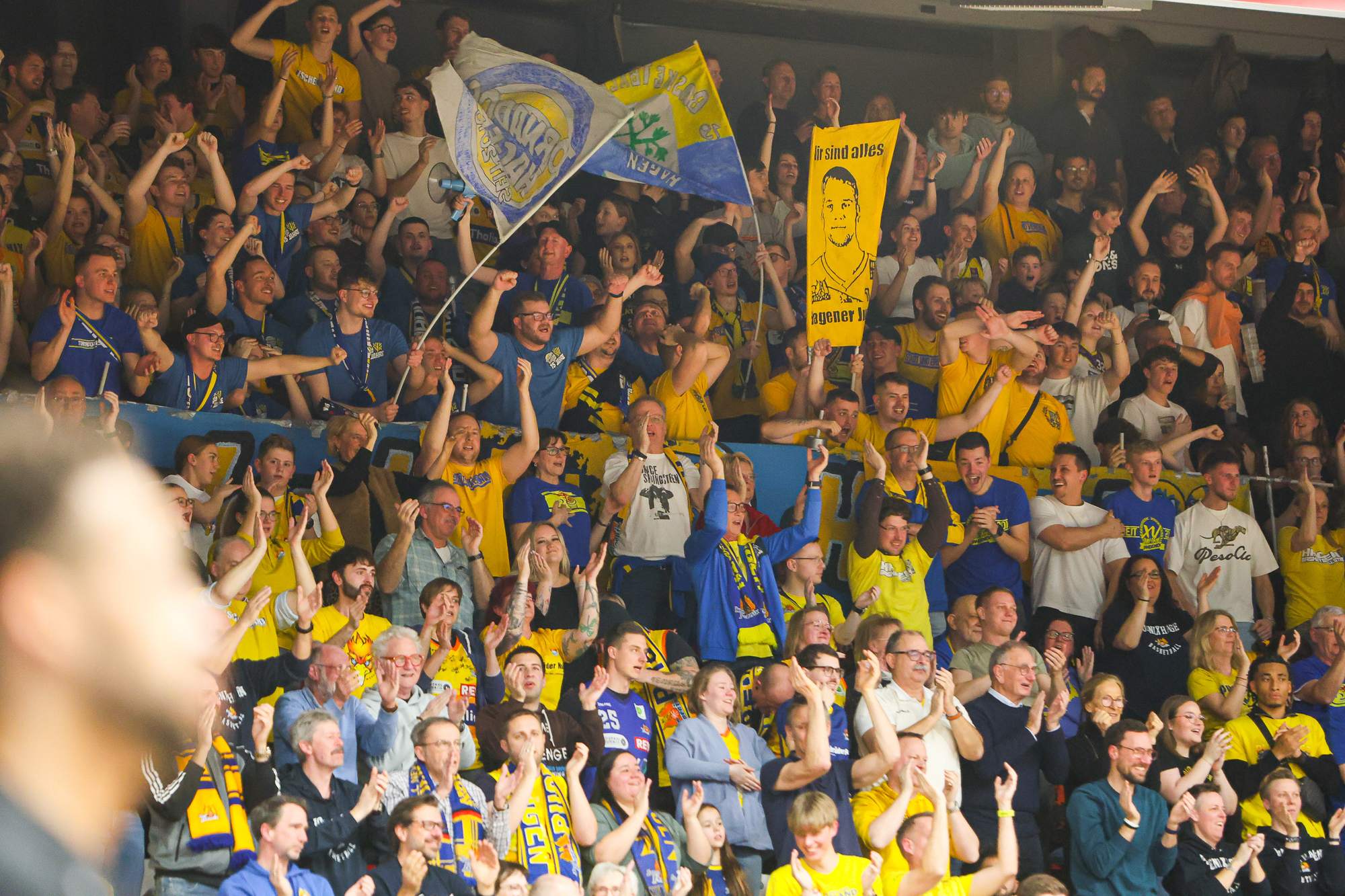 Jubelnde Menge in gelbblauer Kleidung mit Fahnen und Schildern bei einem Sportevent