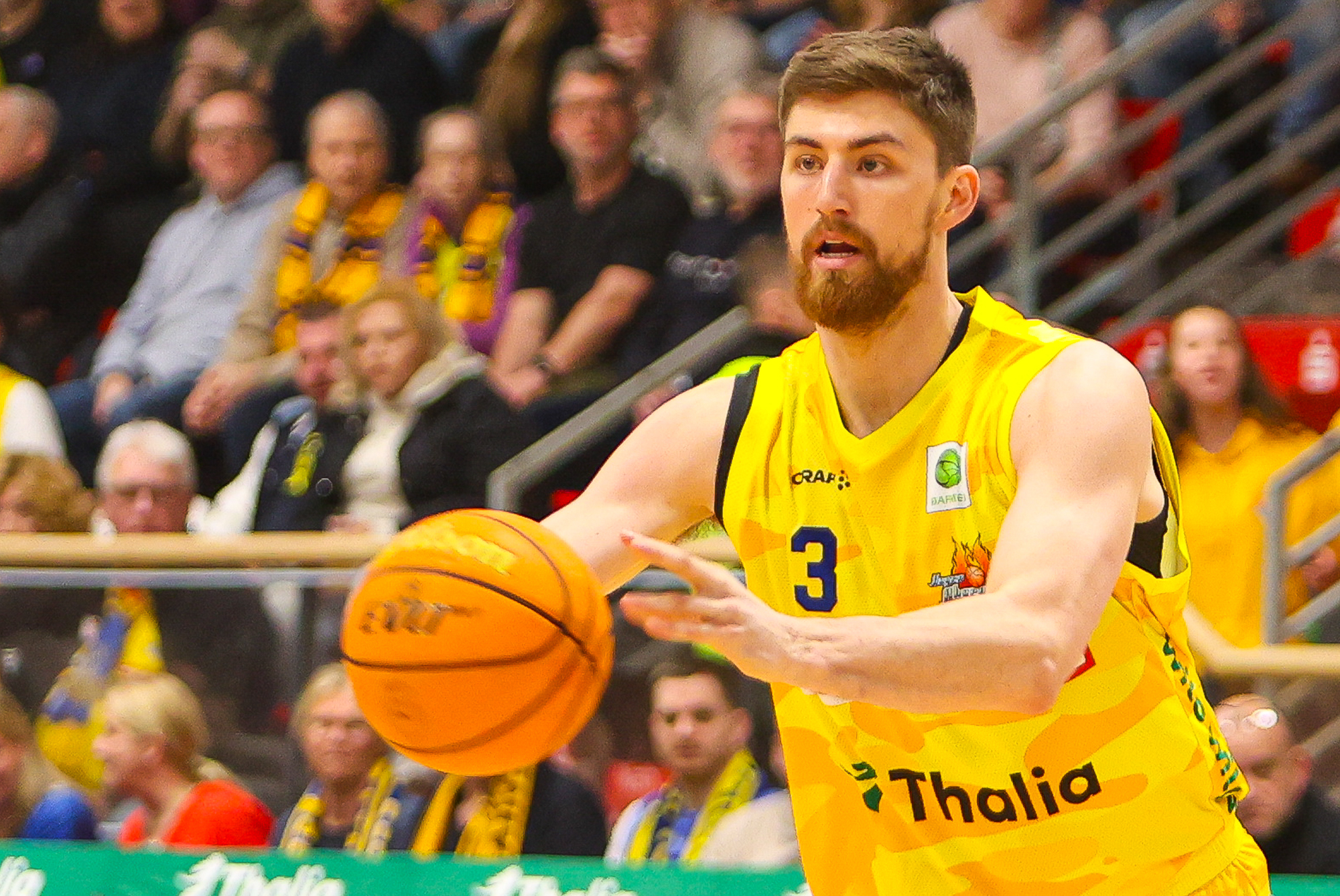 Ein Basketballspieler im gelben Trikot mit Bart passt konzentriert den Ball