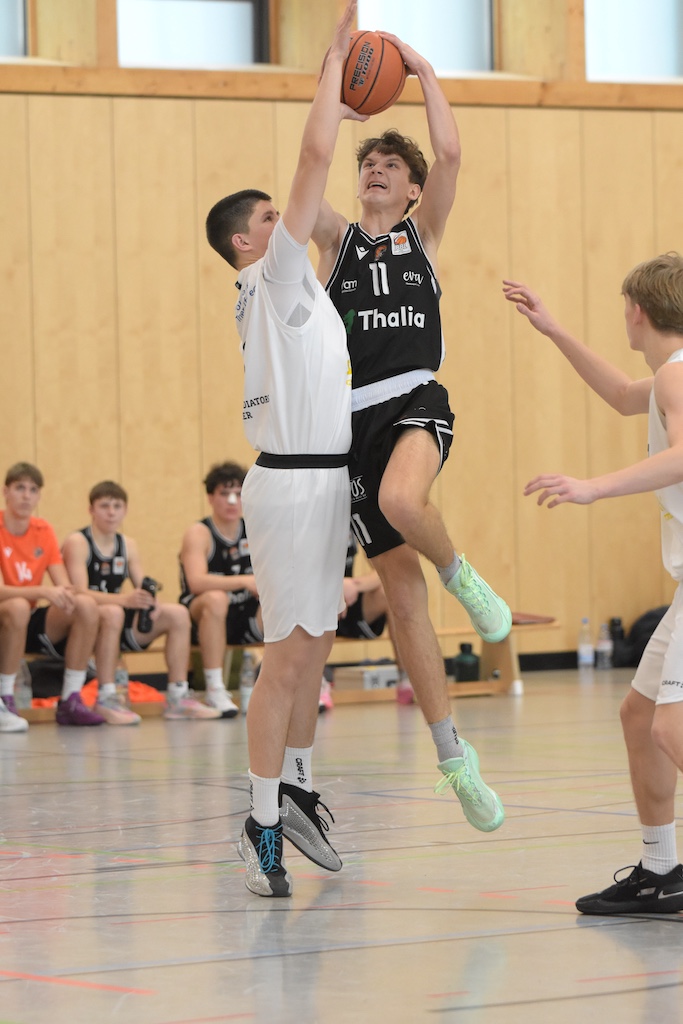 Zwei jugendliche Basketballspieler im Spiel, einer springt mit entschlossenem Gesichtsausdruck zum Korb