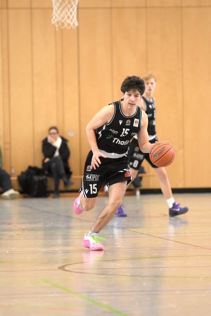 Ein junger Basketballspieler im schwarzen Trikot dribbelt konzentriert auf dem Spielfeld