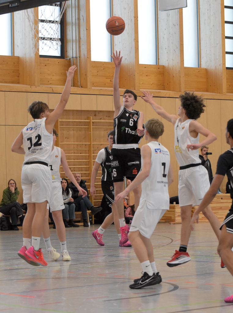 Ein junger Basketballspieler im schwarzen Trikot wirft konzentriert den Ball zum Korb
